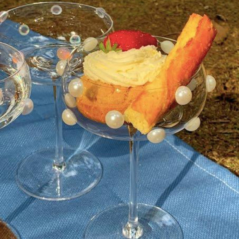 Luxury design cocktail coupette glasses. Dessert in a glass with whipped cream, strawberries, and cookies on a blue cloth.